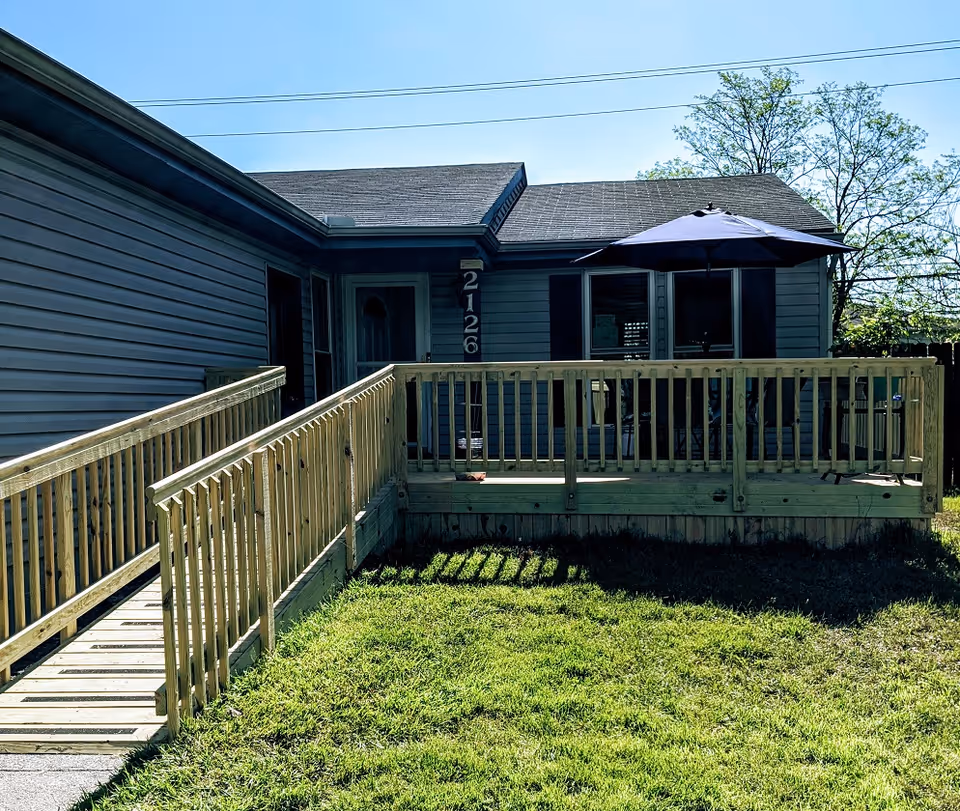 Blue single-story senior care home exterior with ramp and umbrella on deck.