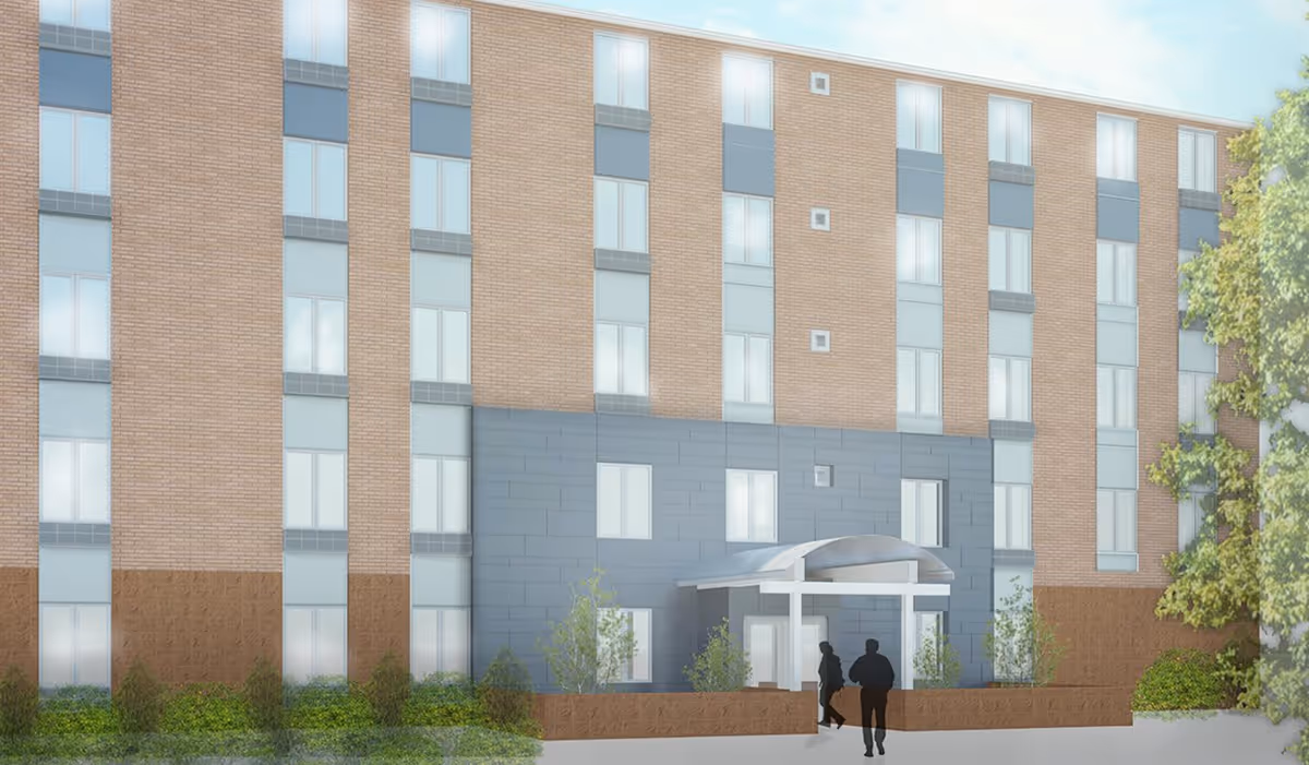 Front exterior of a multi-story brick senior living building with a covered entrance and two silhouetted people walking toward it.