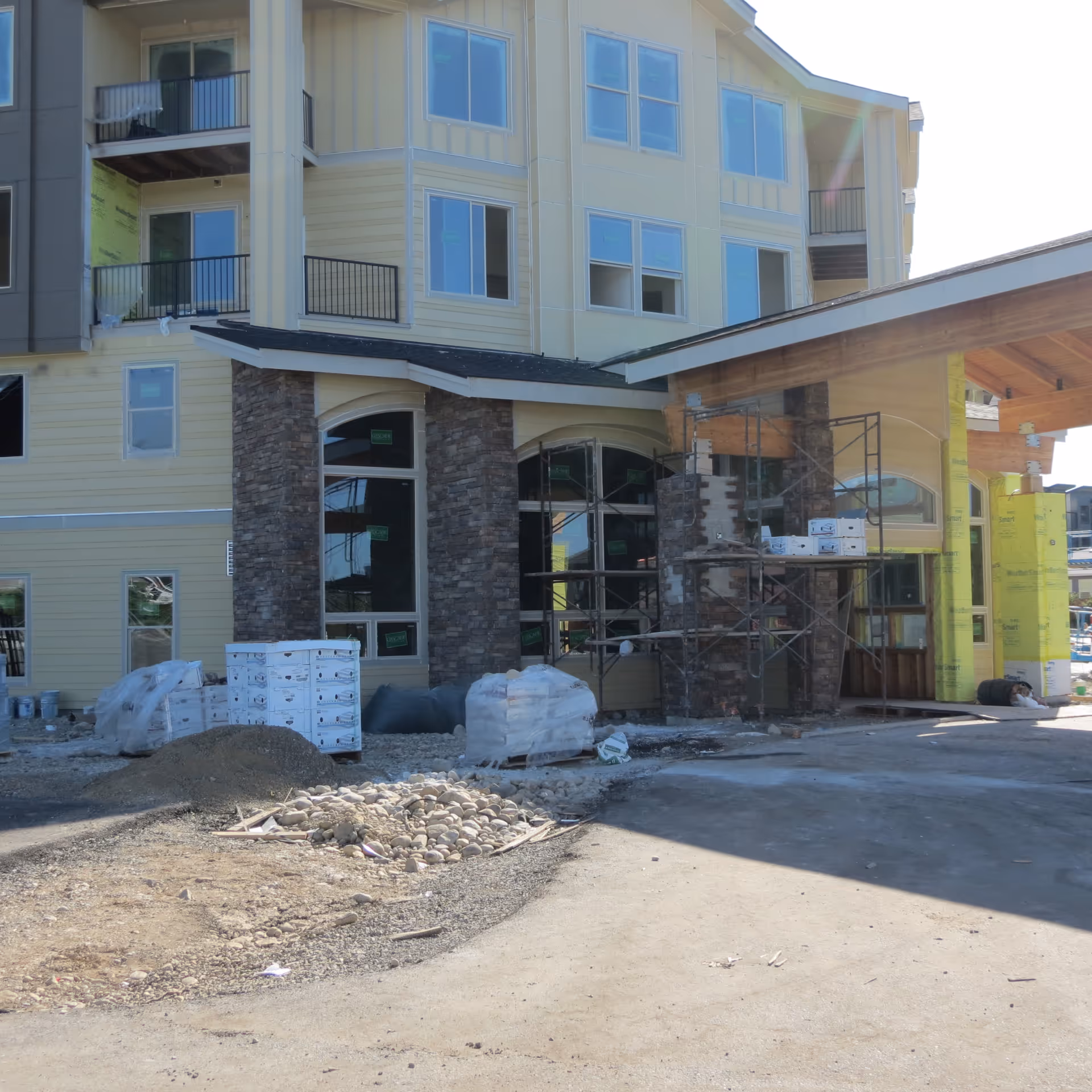 Front entrance of a multi-story senior living building under construction with scaffolding and construction materials in the driveway.