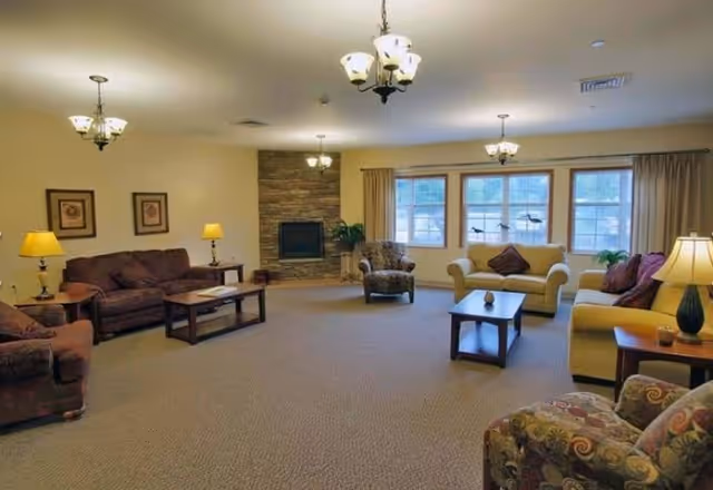 Spacious communal living room with sofas, armchairs, coffee tables, lamps and a stone fireplace under ceiling chandeliers.