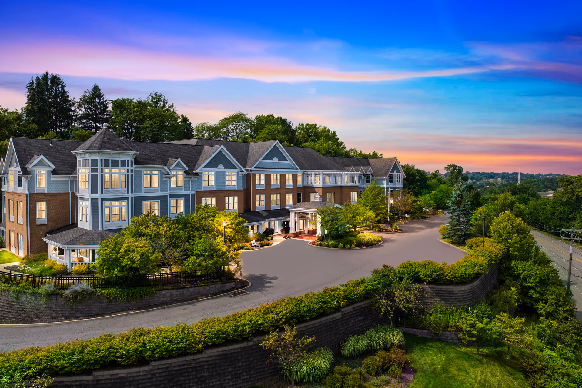 Exterior view of a multi-wing senior living facility with landscaped entrance and sunset sky.
