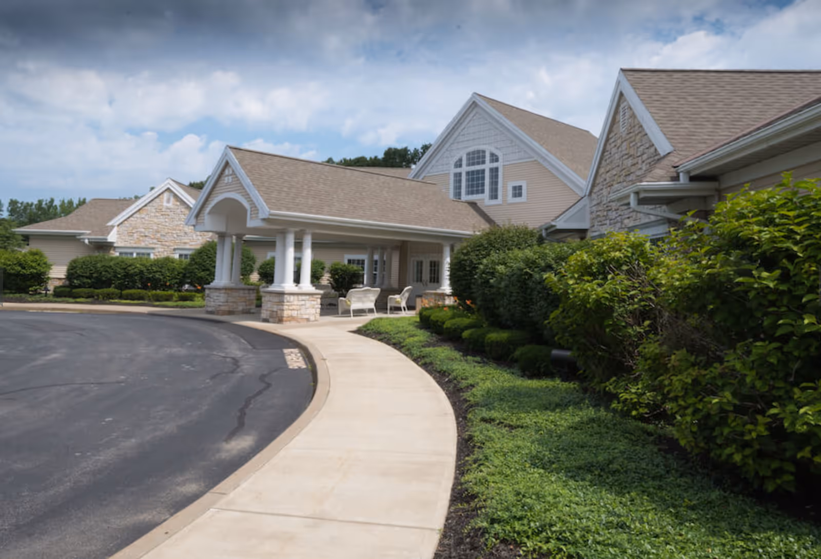 Exterior view of a senior living facility with a curved pathway and landscaped greenery.