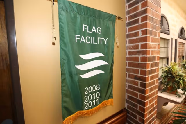 A green "Flag Facility" banner listing years 2008, 2010, 2011 hangs on an interior wall next to a brick column and windows.