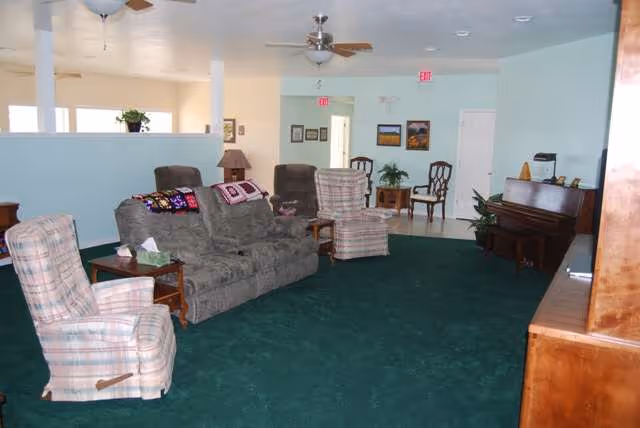 Spacious living room in Serenity House Assisted Living with couches, chairs, piano, and plants.