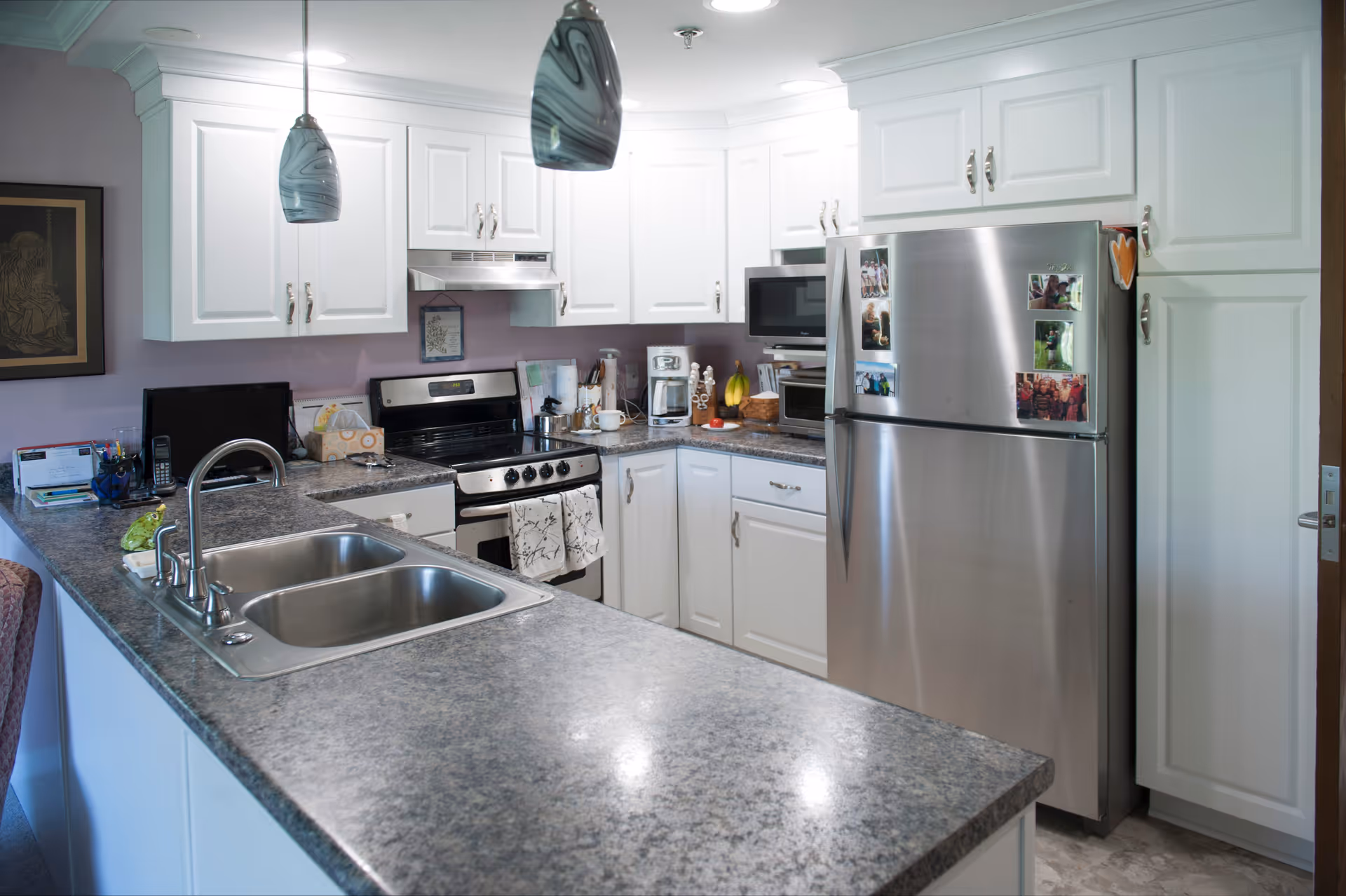 Bright modern kitchen with white cabinets, stainless steel refrigerator and stove, and a large countertop with a double sink.