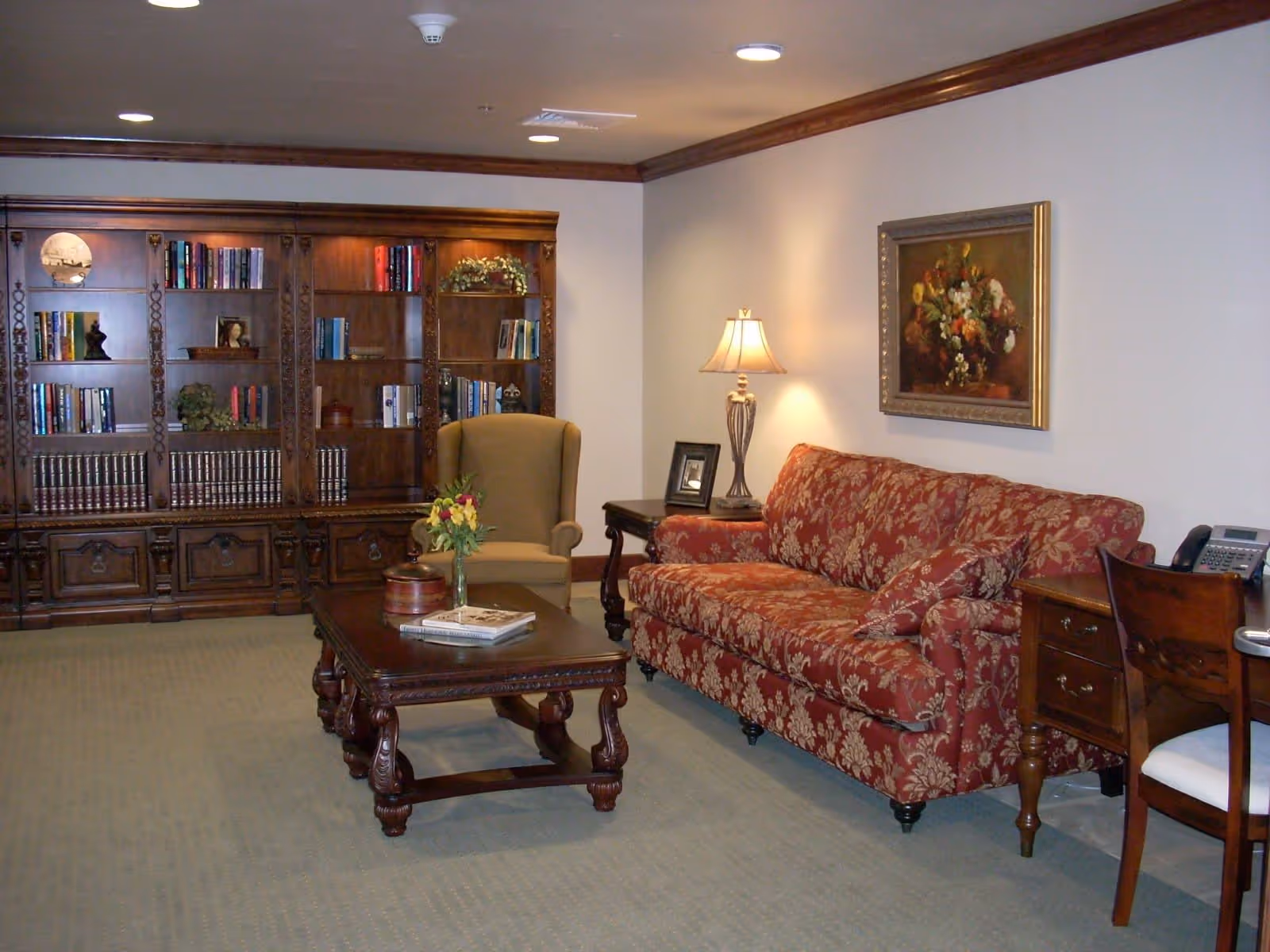 A cozy lounge with a patterned red sofa, armchair, wooden coffee table and a large built-in bookcase.