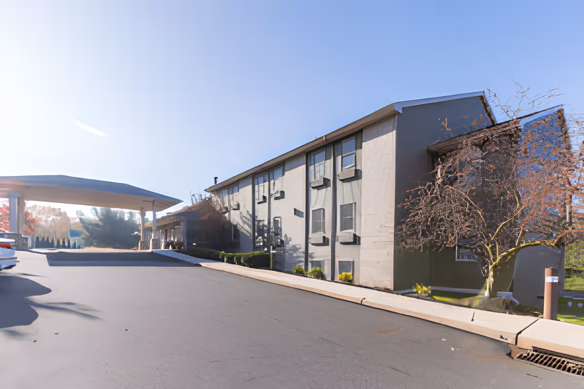 Front exterior of a multi-story senior living building with a covered drop-off canopy and driveway.