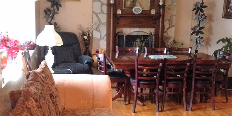 Cozy living/dining room with a wooden dining table and chairs in front of a fireplace, sofas and a lamp.