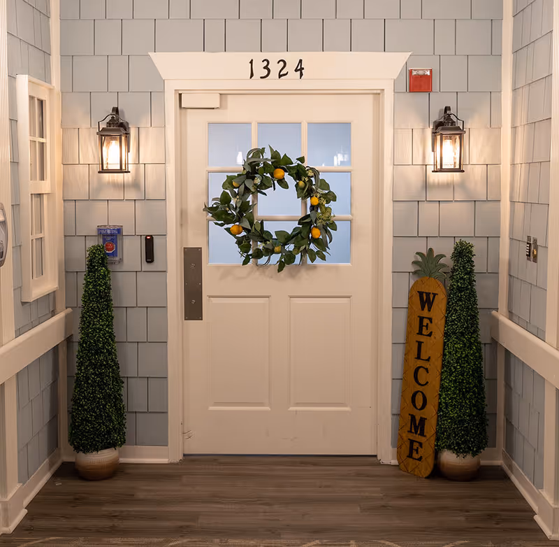 Interior entry door decorated with a lemon wreath flanked by lanterns, topiary plants, and a 'WELCOME' sign beneath the number 1324.