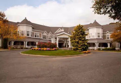 A large senior living facility with circular driveway and landscaped center, front entrance visible.