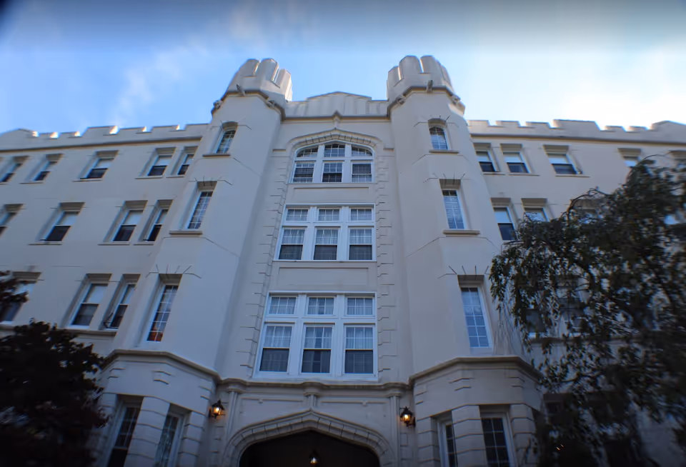 Front facade of a multi-story, castle-style building with turrets and many windows.