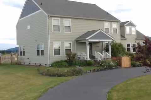 Exterior view of a two-story, light-green senior living home with a front porch and driveway.