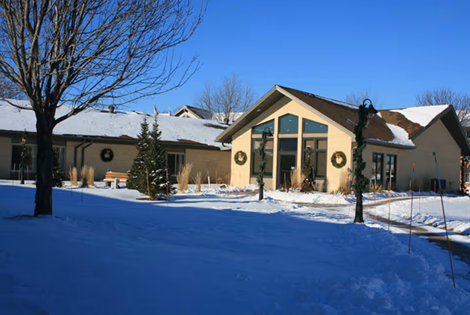 Exterior view of a single-story building with a snow-covered roof and ground, decorated with Christmas wreaths and garlands on lamp posts, under a clear blue sky.