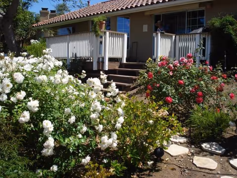 Senior living facility front exterior with white railing, steps, and blooming rose bushes.