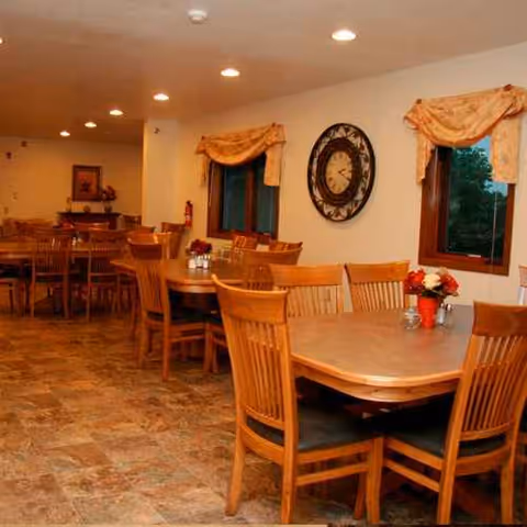 Wooden tables and chairs arranged in a well-lit dining room with windows.