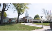 Front exterior of a single-story brick healthcare building with a covered entrance, circular driveway, manicured lawn, trees, and a white cupola.