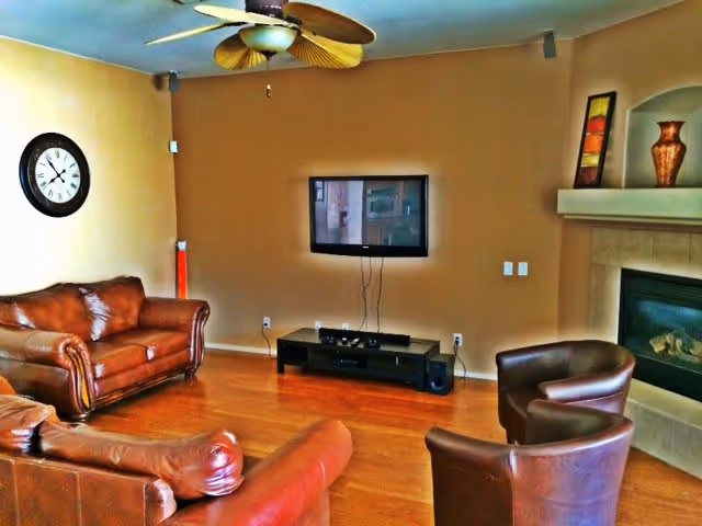 Cozy living room with leather sofas and chairs, a wall-mounted TV, ceiling fan, and a fireplace.