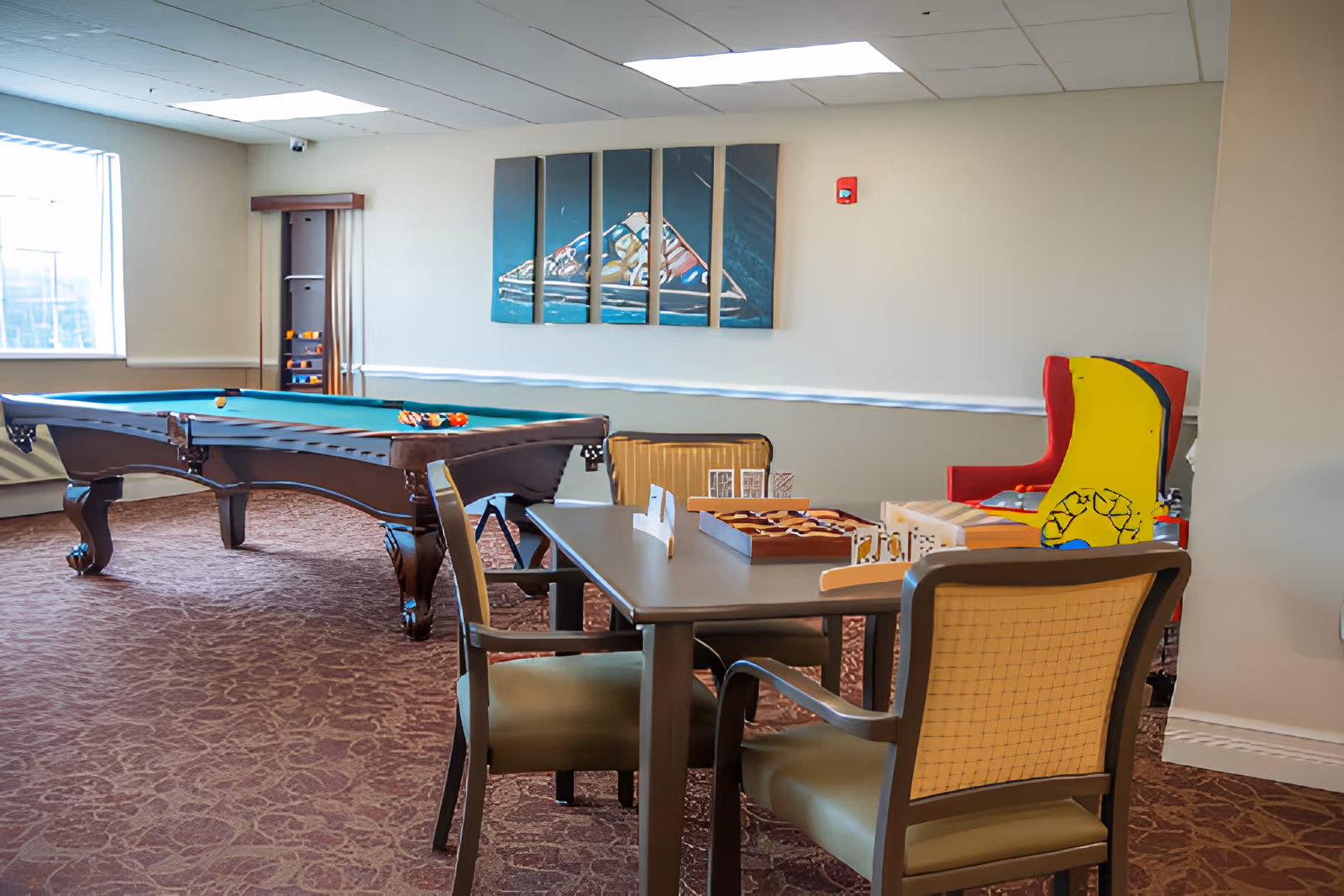 Recreation room with a pool table, a game table with chairs, and colorful armchairs beneath wall art.