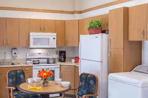 Cozy kitchen area with wooden cabinets, refrigerator, stove, microwave, and a small dining table.