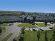A senior living campus building with a circular driveway, manicured lawn, and parked cars.