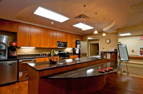 Modern kitchen area with curved island, dark granite countertops, and wooden cabinetry.