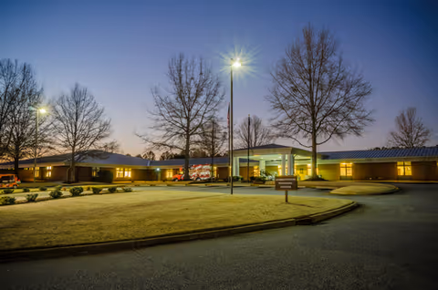 Exterior view of a single-story veterans nursing home at dusk with a lit entrance and bare trees nearby.