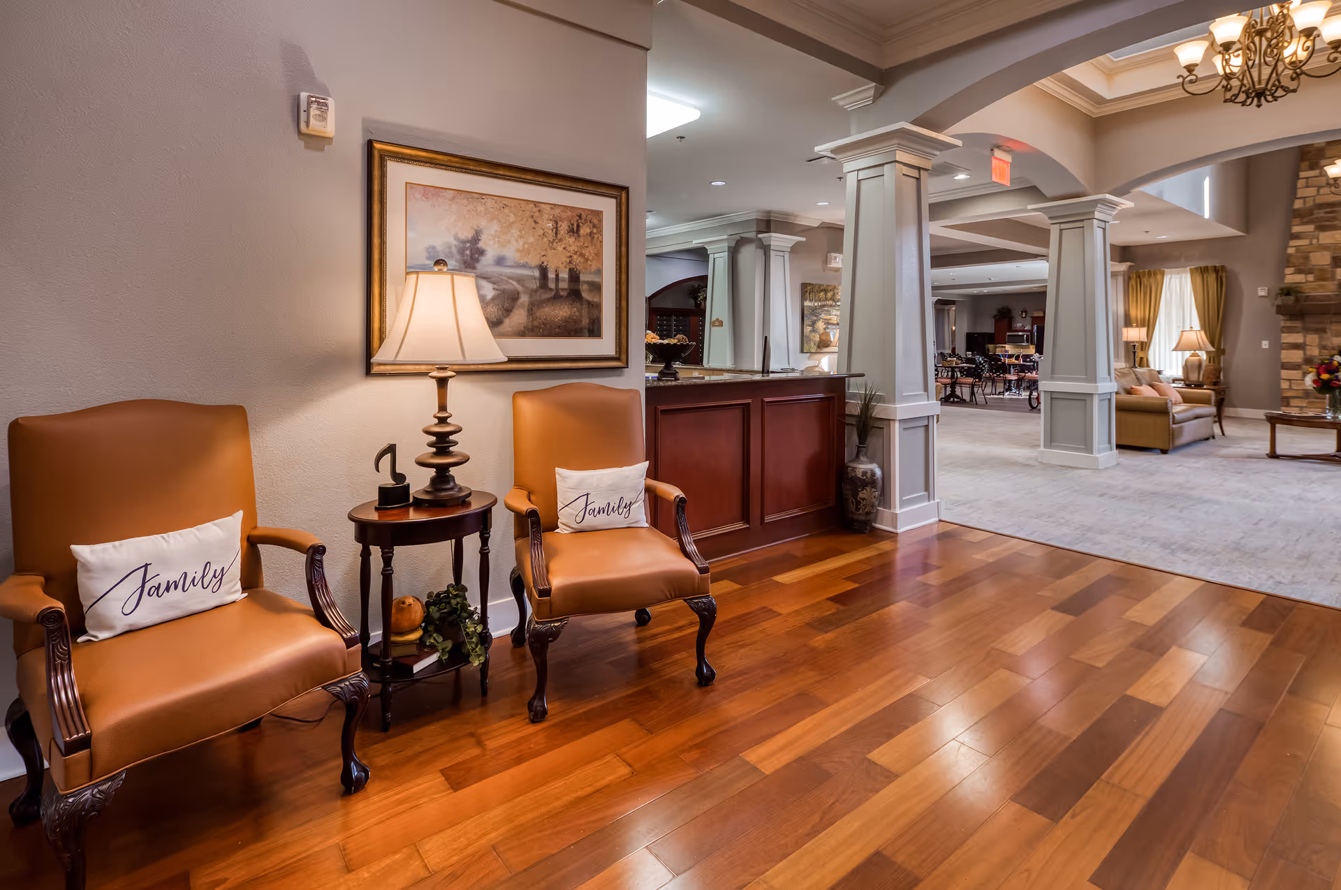 Spacious assisted living lobby with two leather armchairs and a side table in the foreground and an open lounge and reception area beyond.
