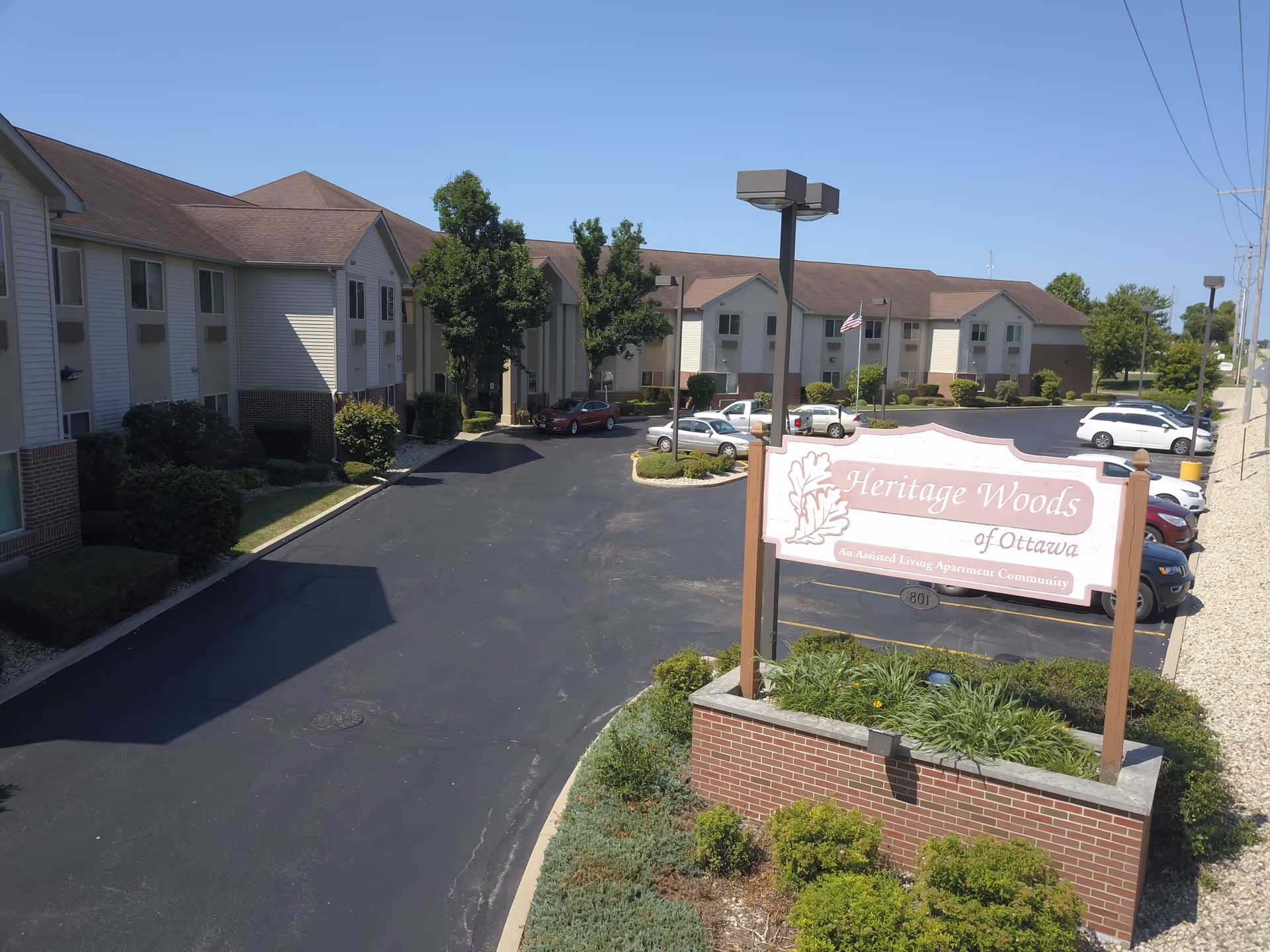 Front exterior view of the Heritage Woods of Ottawa assisted living complex showing the entrance sign, parking lot, and two-story buildings.