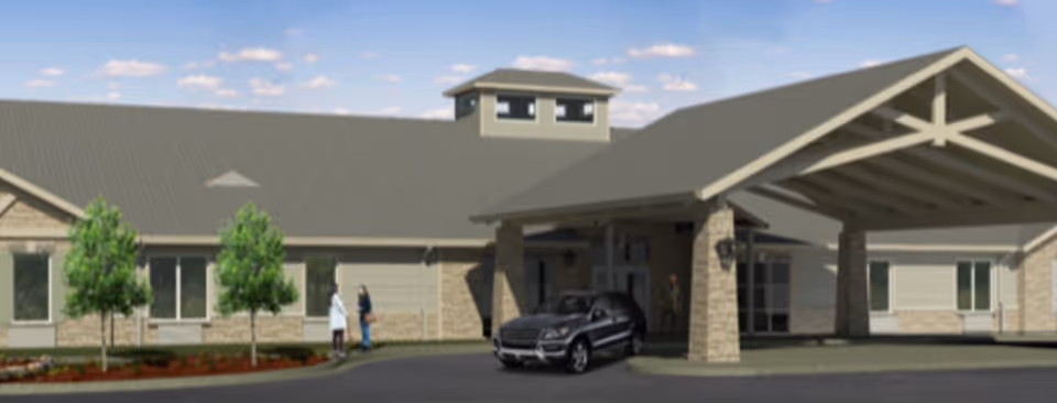 Exterior view of a single-story senior living facility building with a covered entrance supported by stone pillars. There are a few small trees and landscaping in front, a black SUV parked under the entrance, and two people standing near the building.