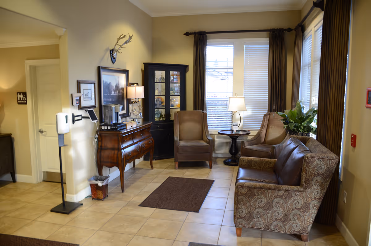 Cozy sitting area with a leather sofa, two armchairs, a wooden sideboard, and windows with curtains.