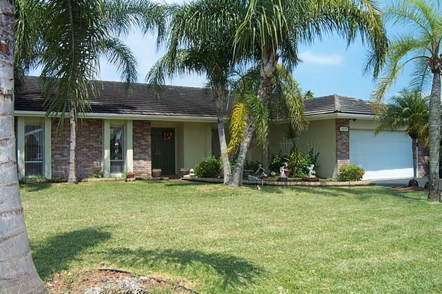 Single-story assisted living facility with brick facade, palm trees, and a green lawn.