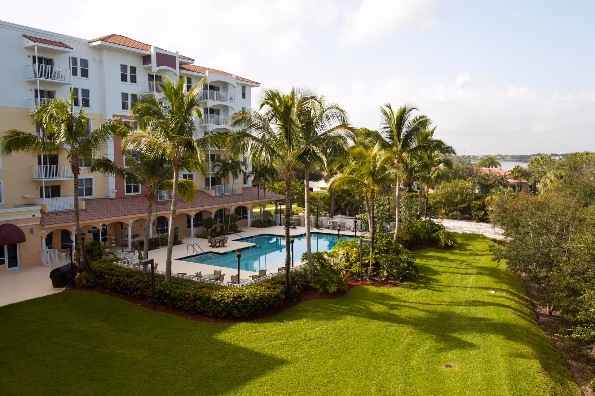 Courtyard view of Mangrove Bay showing a swimming pool, palm trees, green lawn, and an adjacent multi-story building.