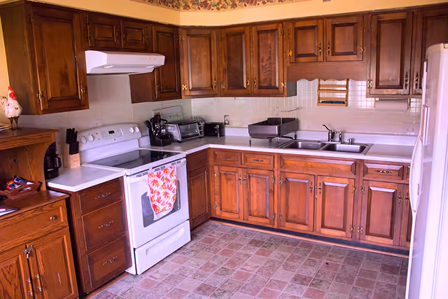 A traditional kitchen with dark wooden cabinets, white countertops, a white stove with a floral towel, and a double sink.