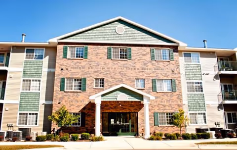 Three-story brick senior living building with green shutters and a covered entrance.