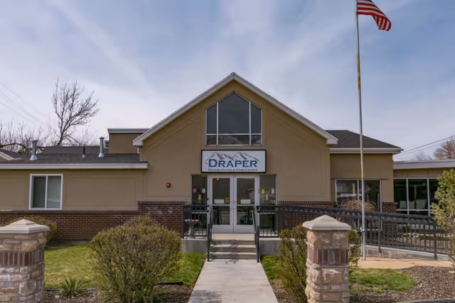 Front entrance of Draper Rehabilitation and Care Center building with a walkway, steps, and an American flag.