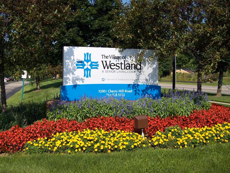 Entrance sign for The Village of Westland surrounded by colorful flower beds and trees.
