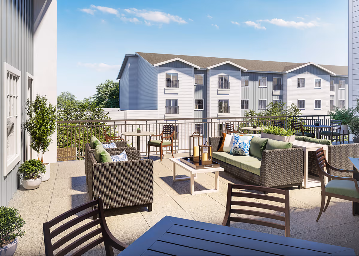 Outdoor terrace with wicker seating, cushioned sofas, tables and potted plants overlooking nearby apartment buildings.