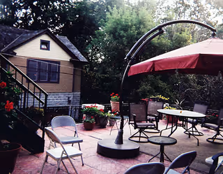 Outdoor patio with tables, chairs, potted plants, and a large umbrella beside a building.