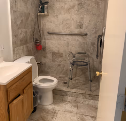 Accessible bathroom with toilet, sink, walk-in shower, and a walker near the door.