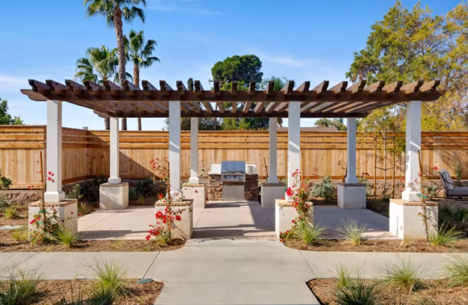 Pergola-covered outdoor grilling area with columns, a built-in barbecue, and a wooden fence backdrop.