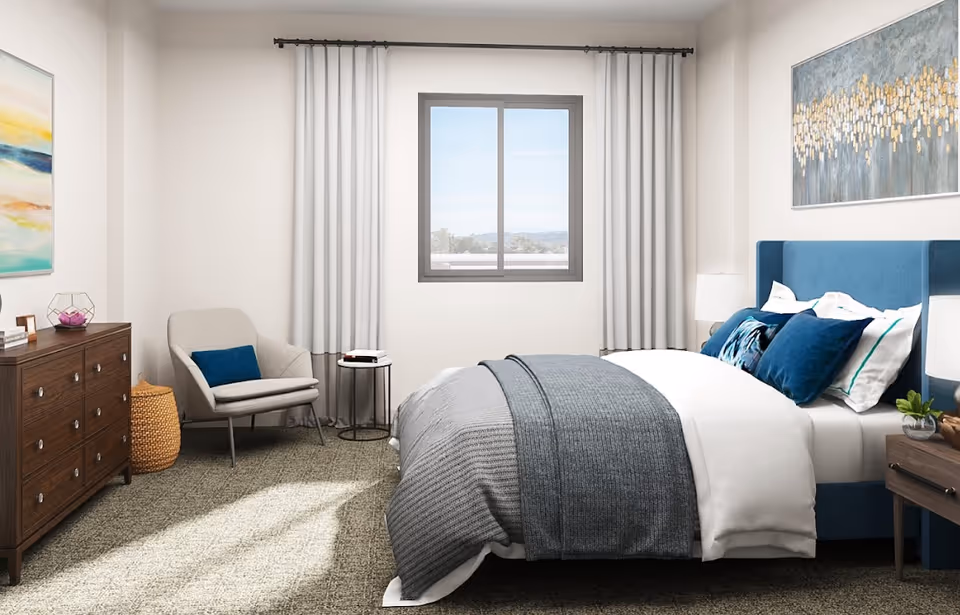 Bright modern bedroom with a blue upholstered bed, gray bedding, an armchair, dresser, and a window with curtains.