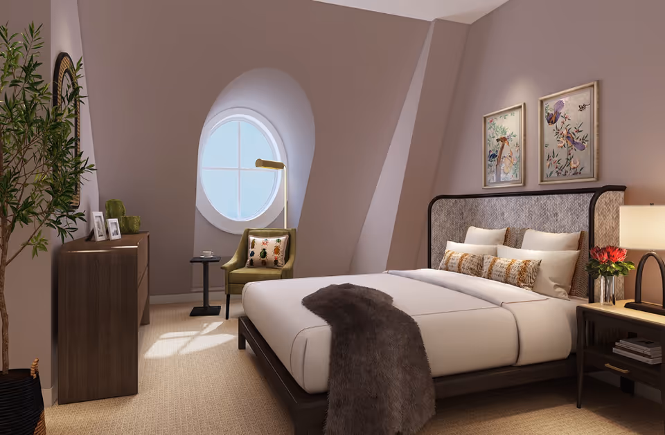 Cozy bedroom with a large bed, round window, armchair, dresser, and bedside table with a lamp and flowers.