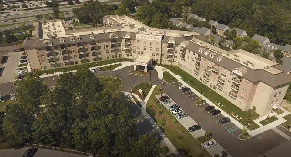 Aerial view of the Woodland Terrace of Carmel senior living building with a curved entrance drive, parking lot, and surrounding trees.