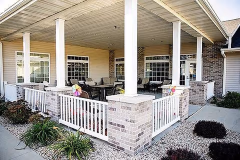Covered outdoor patio with white columns, brick half-walls and railing, furnished with tables and chairs and decorative pinwheels.