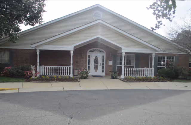 Front entrance of a single-story brick building with a covered porch, white columns, and a central glass door.