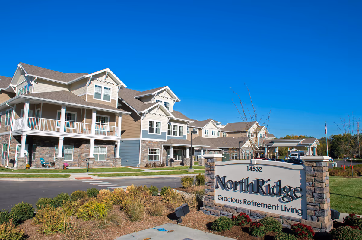 Exterior of a multi-story senior living building with landscaping and a stone sign reading "NorthRidge Gracious Retirement Living" in the foreground.