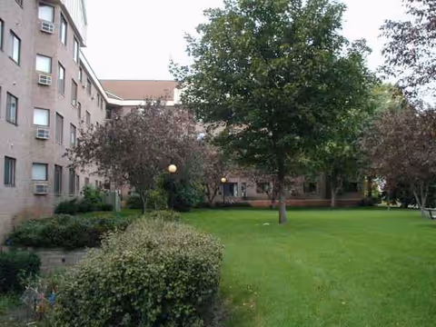 Brick Copperfield Hill building with green lawn, trees, and shrubs in courtyard.