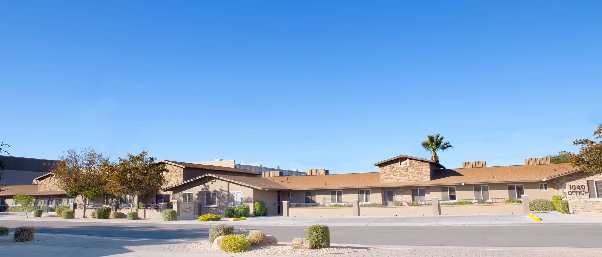 Front exterior of a single-story assisted living facility with desert landscaping under a clear blue sky.