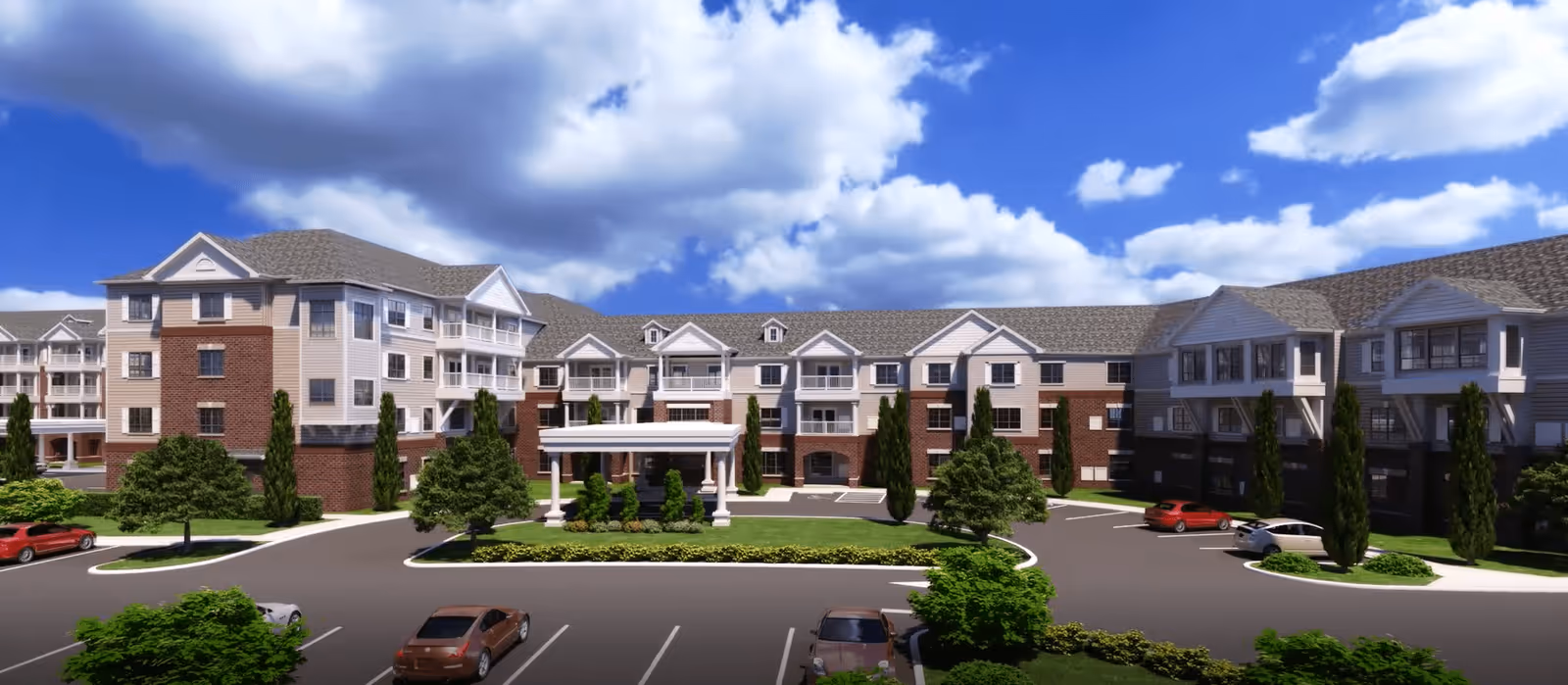 Exterior view of a large senior living facility named Harmony at Enterprise, featuring a multi-story building with a combination of brick and light-colored siding, multiple windows, balconies, and a covered entrance. The foreground shows a parking lot with several cars and landscaped greenery including trees and shrubs under a partly cloudy blue sky.