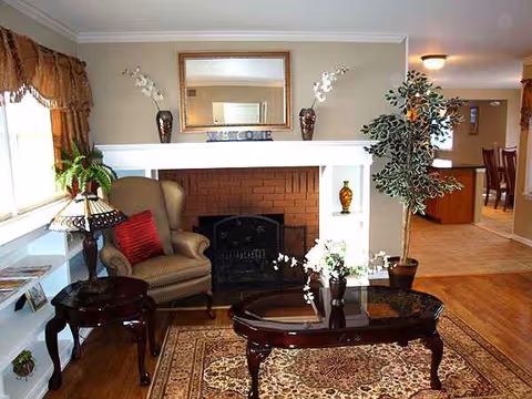 Cozy living room with fireplace, mantle, mirror, armchairs, coffee table, rug, and plants at Comfort's Place.